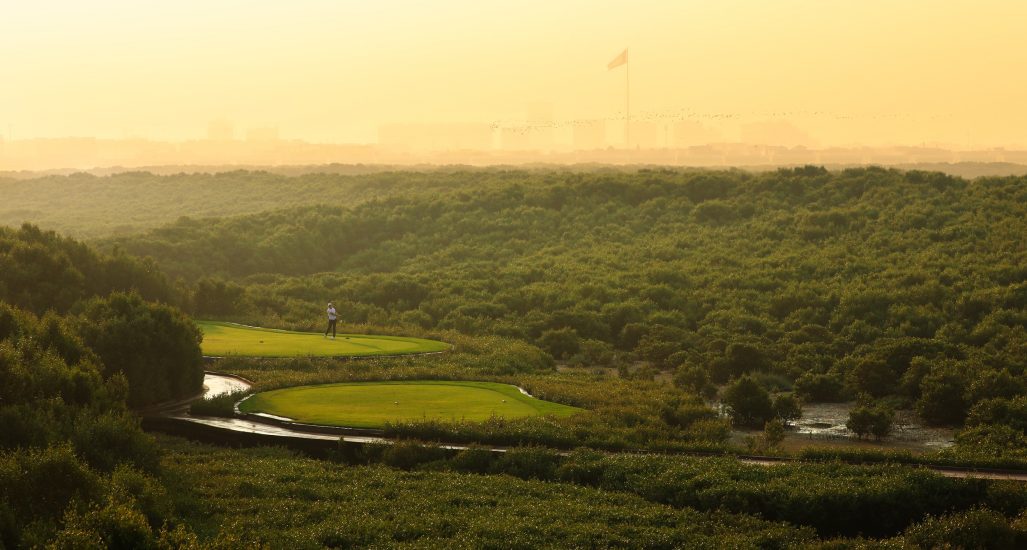 Aerial view golfer tees off on hole 16 at Al Zorah Golf Club surrounded by mangroves